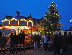 Weihnachtsmarkt mit Karussell und beleuchtetem Weihnachtsbaum bei Nacht.