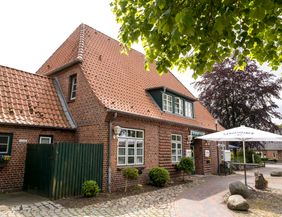 Ein traditionelles Backsteingebäude mit rotem Ziegeldach und einem Gerolsteiner Sonnenschirm im Vordergrund.