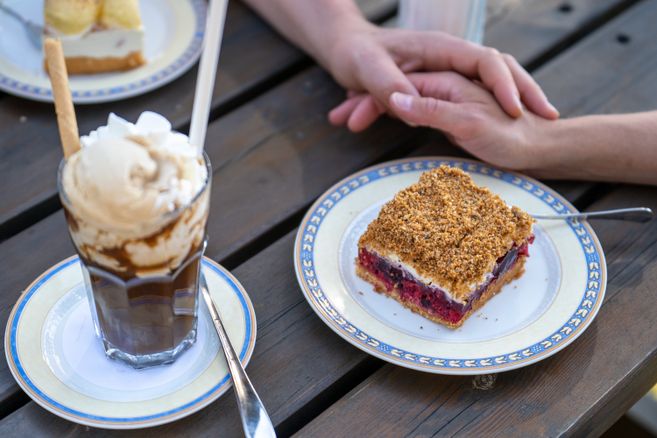 Ein Kuchen und eine Eisschokolade liegen auf einem Tisch. Zwei Hände liege