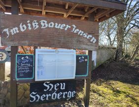 Hölzernes Willkommensschild mit Informationen zum Imbiss und Zeltplatz Bauer Jensen