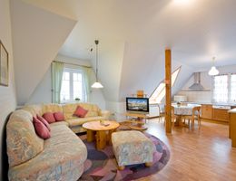 Gemütliches Wohnzimmer mit Ecksofa, Fernseher und offener Küche in einer Dachgeschosswohnung.