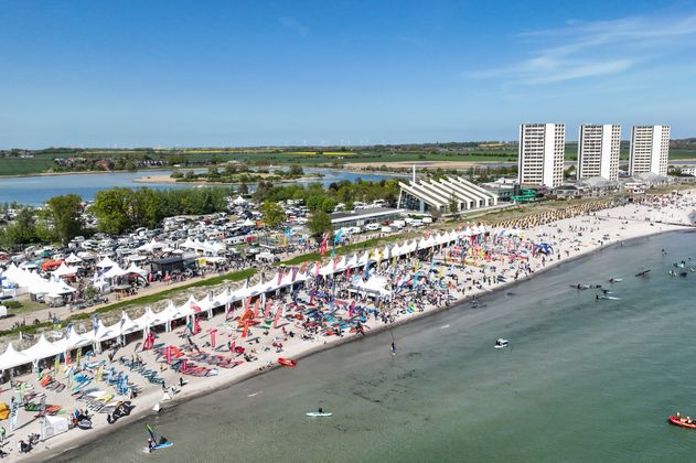 Luftaufnahme eines Strandes mit Surffestival, Zelten und vielen Menschen.