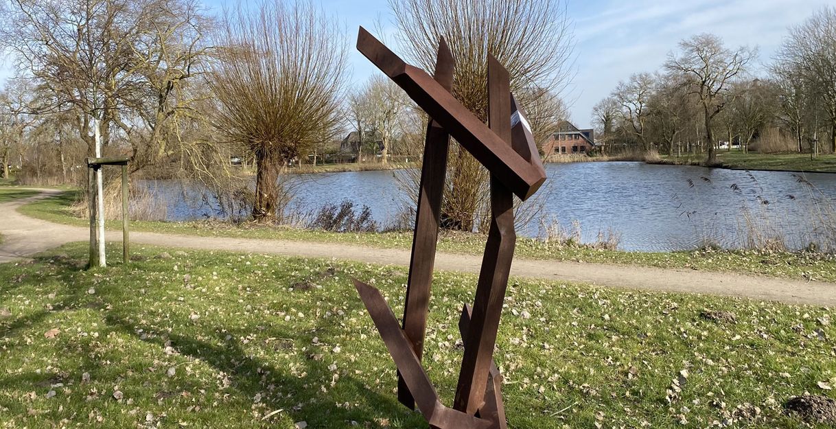 Moderne Skulptur aus Metall vor einem Teich in einer Parklandschaft.
