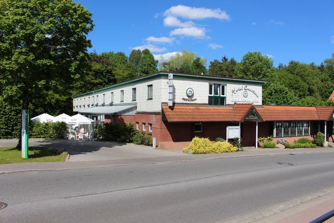 Außenansicht eines Hotels mit Restaurant und Terrasse, umgeben von Bäumen.