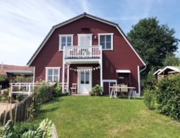 Ein rotes, zweistöckiges Haus mit weißem Balkon und Garten im Vordergrund.