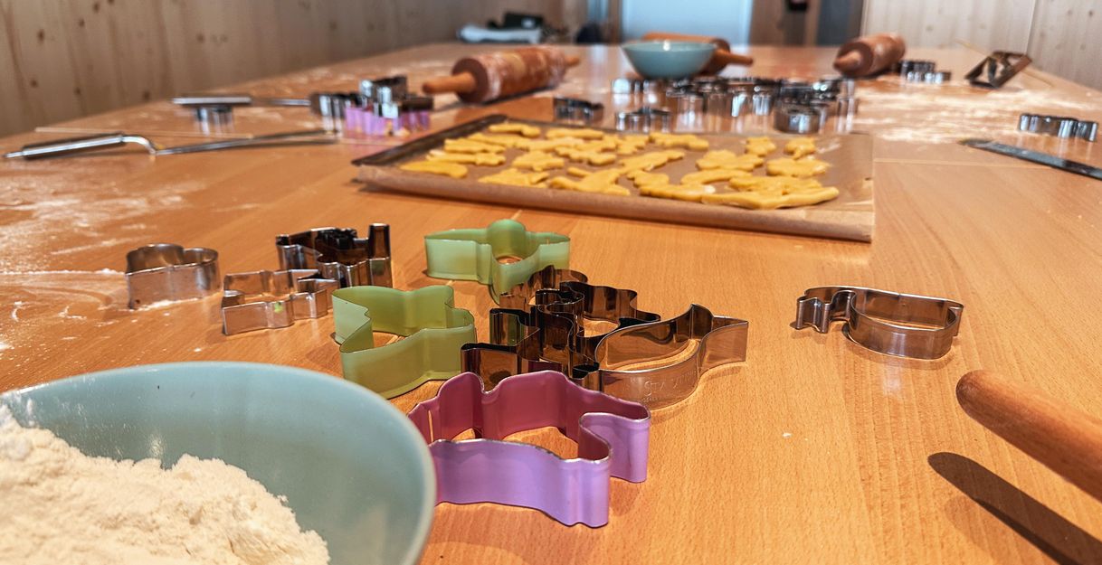 A kitchen countertop with cookie cutters in various colors. Dough and baking utensils are also spread out on the table.