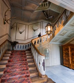 Eine historische Treppe mit rotem Teppich und Geweihen an der Wand