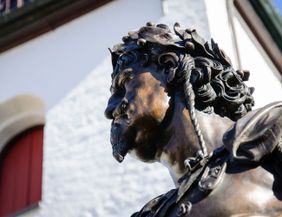 Nahaufnahme einer Bronzestatue mit Lorbeerkranz vor einem Gebäude.