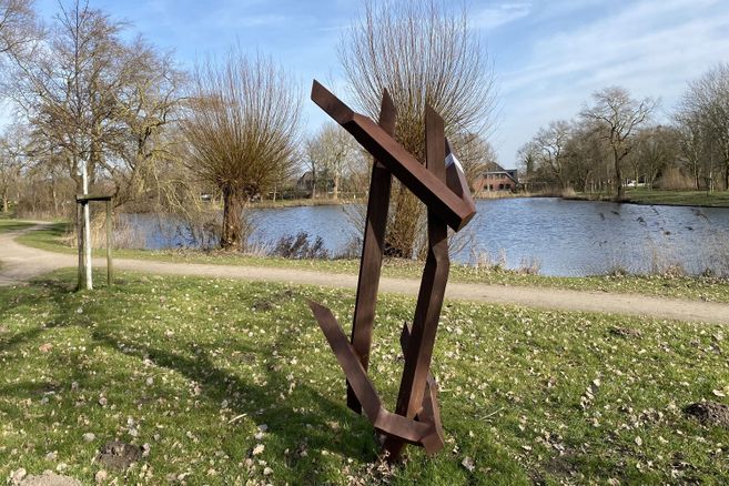 Moderne Skulptur aus Metall vor einem Teich in einer Parklandschaft.