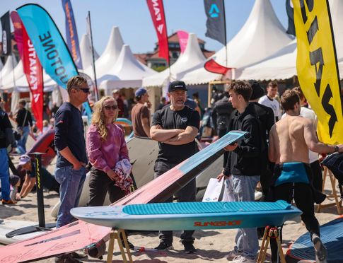 Menschen auf einem Surf-Festival mit Surfbrettern und Zelten im Hintergrund.