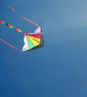 A colorful kite soars high in the clear blue sky. The long, colorful ribbons flutter in the wind.