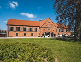 Hotel Breitenburg: historisches Backsteingebäude mit rotem Dach, davor eine große grüne Wiese und geparkte Autos.