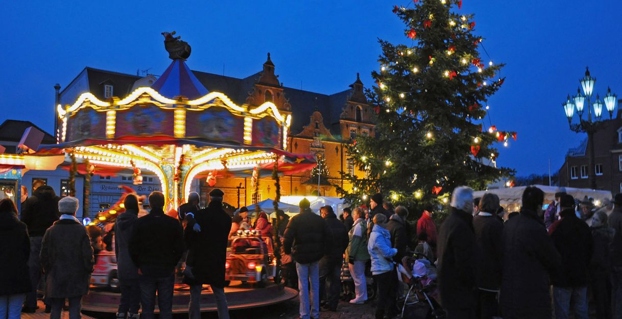 Weihnachtsmarkt mit Karussell und beleuchtetem Weihnachtsbaum bei Nacht.