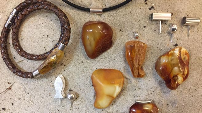 Eine Sammlung von Schmuckstücken aus Bernstein, darunter Ohrringe, Anhänger und ein Armband. Die Schmuckstücke haben verschiedene Formen und sind in warmen Erdtönen gehalten.