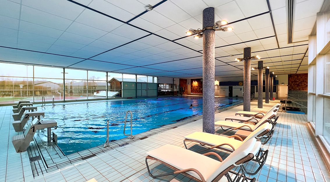 Innenansicht eines Hallenbads mit Schwimmbecken und Liegestühlen.