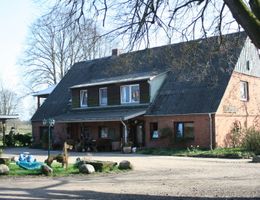 Landhaus mit großem, steilem Dach, roter Backsteinfassade und Vorgarten; links steht ein Auto, im Vordergrund Spielzeug und Steine.