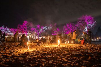 Lichtermeer mit Feuerkörben am Strand von Heikendorf/Möltenort. Bunte Lichtstrahler in den Bäumen.