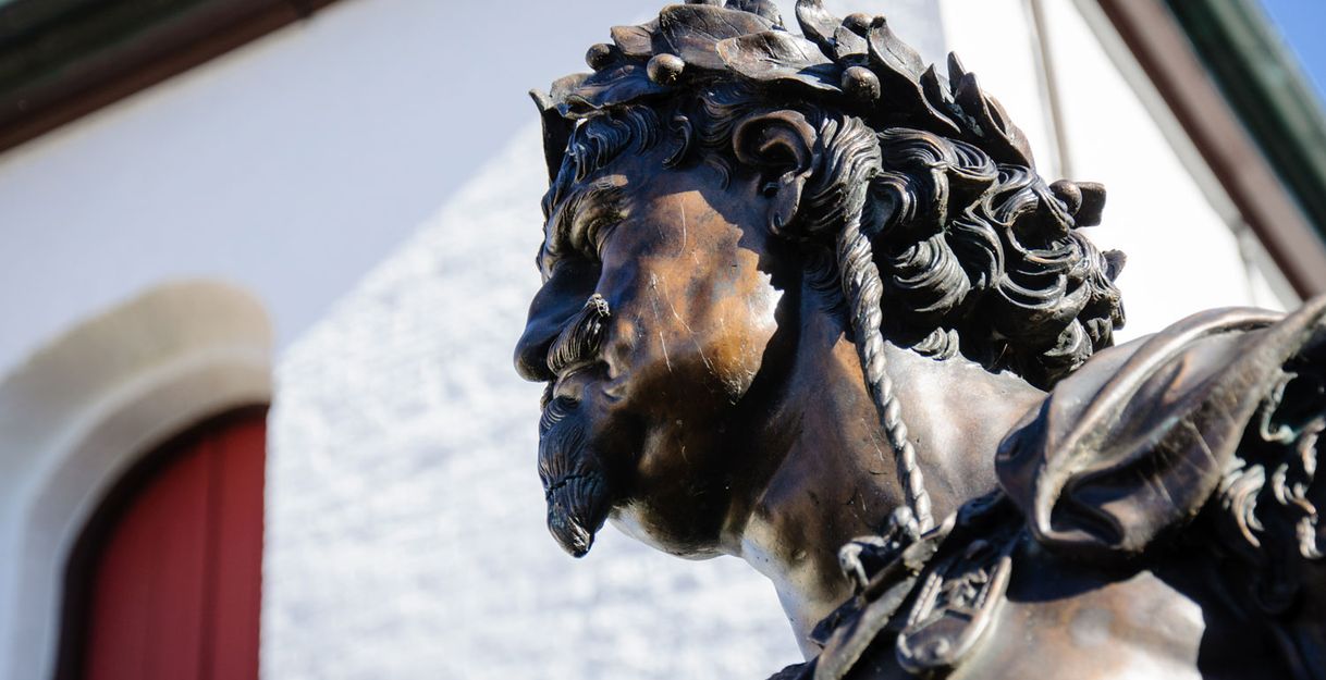 Nahaufnahme einer Bronzestatue mit Lorbeerkranz vor einem Gebäude.