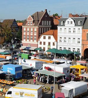 Wochenmarkt mit Verkaufsständen und historischen Gebäuden im Hintergrund.