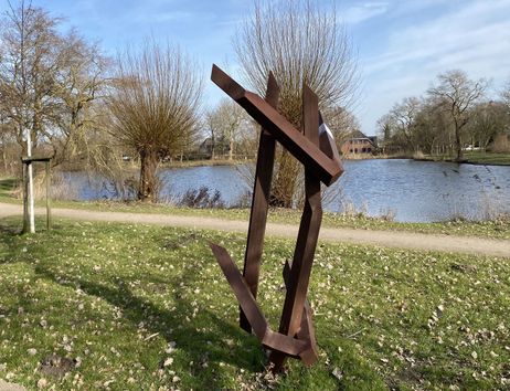 Moderne Skulptur aus Metall vor einem Teich in einer Parklandschaft.