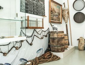 Museumsausstellung mit Fischernetzen, Fässern und maritimen Objekten.