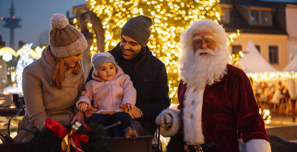 <p>Ein schöner Weihnachtsbaum steht auf einem Marktplatz und im Hintergrund ist eine Kirche im Schnee zu sehen. Der Himmel ist klar und blau, was eine festliche Stimmung schafft.</p>