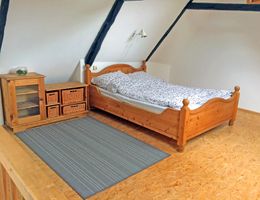 Ein Dachgeschosszimmer mit einem Holzbett, einem Schrank mit Körben und einem grauen Teppich auf Holzboden.