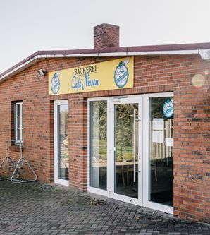 Haupteingang der Bäckerei an einem Backsteinhaus mit Glastüren und Fahrradständer davor