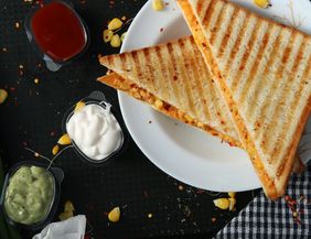 Zwei gegrillte Sandwiches auf einem weißen Teller mit drei verschiedenen Dips daneben.