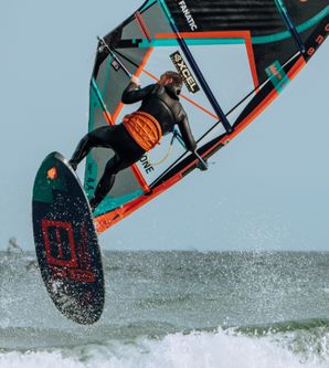 Ein Windsurfer in einem Neoprenanzug springt mit seinem Surfbrett über eine Welle.