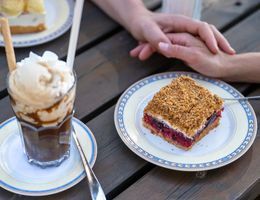 Ein Kuchen und eine Eisschokolade liegen auf einem Tisch. Zwei Hände liege