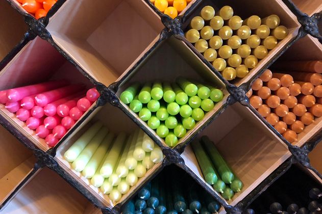 Colorful candles in various shades are neatly arranged in boxes. The colors range from pink to green to black.