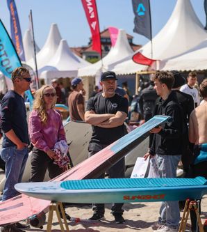 Menschen auf einem Surf-Festival mit Surfbrettern und Zelten im Hintergrund.