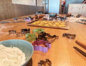 A kitchen countertop with cookie cutters in various colors. Dough and baking utensils are also spread out on the table.