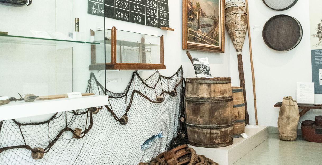 Museumsausstellung mit Fischernetzen, Fässern und maritimen Objekten.