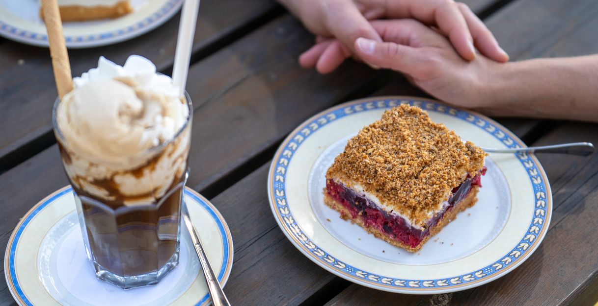 Ein Kuchen und eine Eisschokolade liegen auf einem Tisch. Zwei Hände liegen daneben.