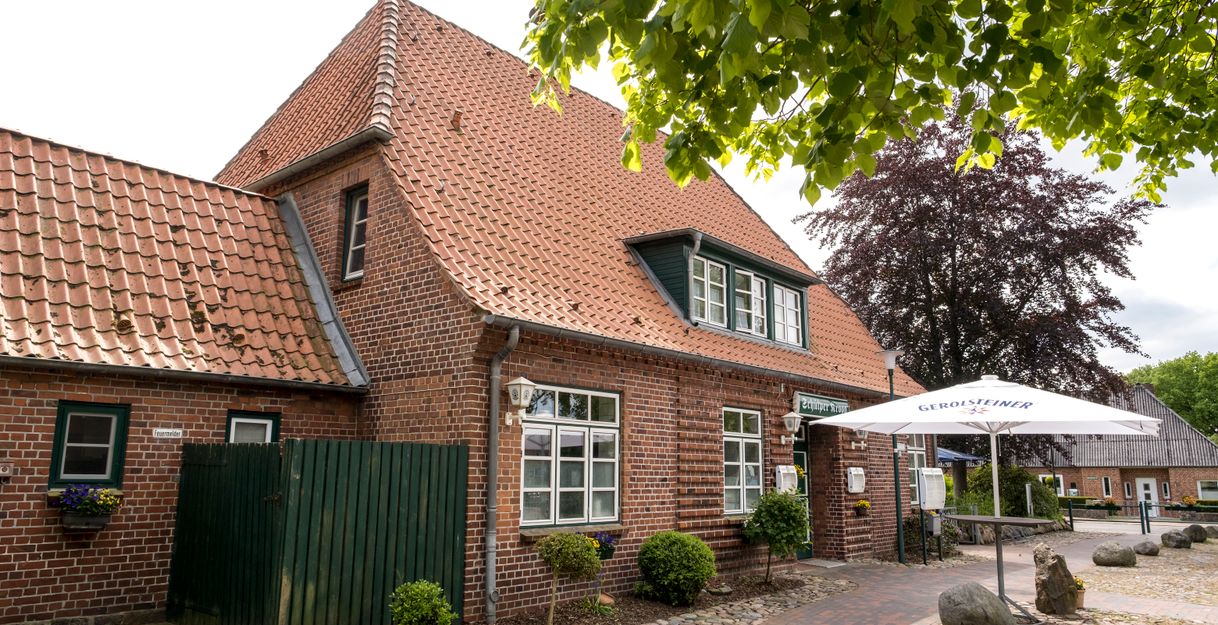 Ein traditionelles Backsteingebäude mit rotem Ziegeldach und einem Gerolsteiner Sonnenschirm im Vordergrund.