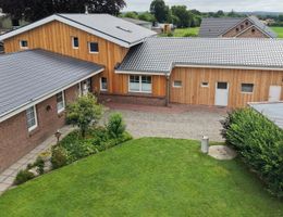 Außenansicht eines Hofes mit mehreren Gebäuden, Holzfassaden, roten Backsteinwänden, grauen Dächern und grünem Garten.