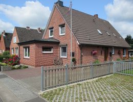 Außenansicht eines roten Backsteinhauses mit Satteldach, Vorgarten und Holzzaun an einer Wohnstraße.