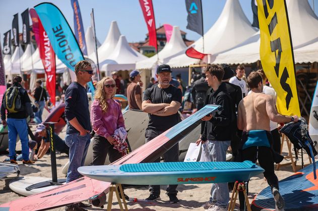 Menschen auf einem Surf-Festival mit Surfbrettern und Zelten im Hintergrund.