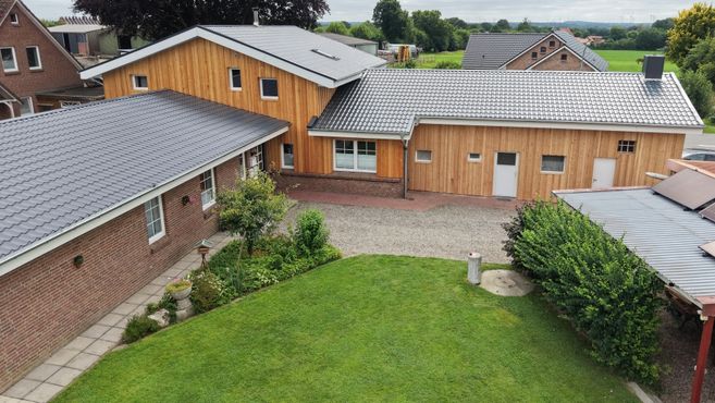 Außenansicht eines Hofes mit mehreren Gebäuden, Holzfassaden, roten Backsteinwänden, grauen Dächern und grünem Garten.