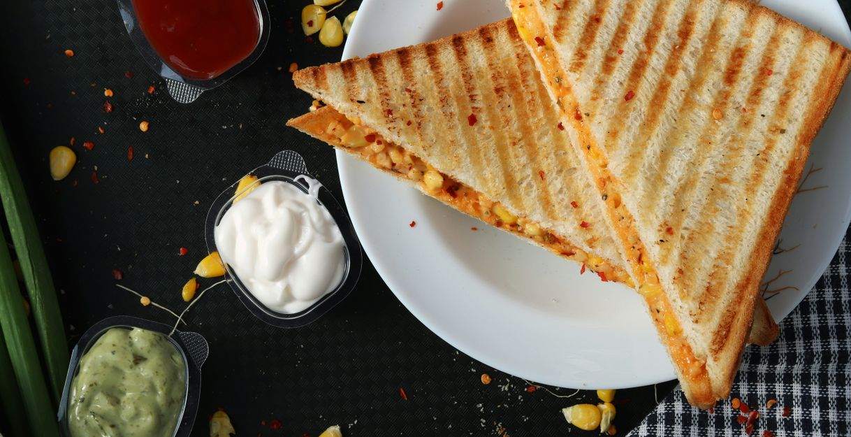 Zwei gegrillte Sandwiches auf einem weißen Teller mit drei verschiedenen Dips daneben.