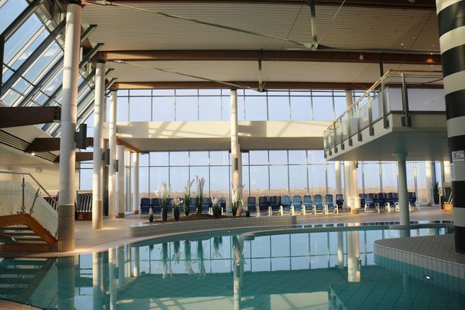 An elegant indoor pool with large windows that let in plenty of natural light. Around the pool, there are loungers and plants for a relaxing atmosphere.