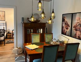 Essbereich mit Holztisch, vier Stühlen, fünf Pendelleuchten und Tierbildern an der Wand; links Blick ins Schlafzimmer.