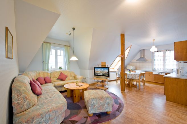 Gemütliches Wohnzimmer mit Ecksofa, Fernseher und offener Küche in einer Dachgeschosswohnung.