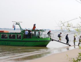 Menschen steigen von einem grünen Boot namens Tidenkieker auf einen Sandstrand aus.