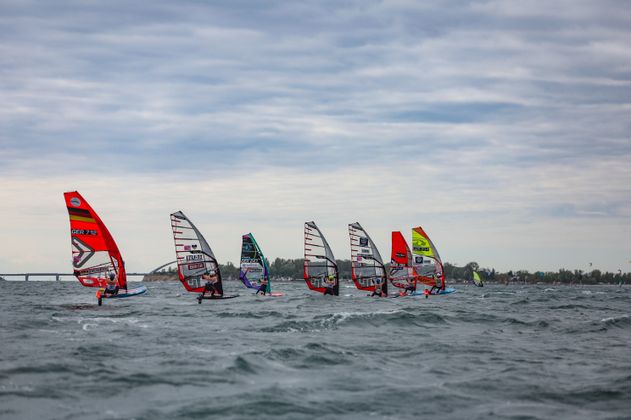 Windsurfer bei einem Rennen auf dem Meer mit bewölktem Himmel.